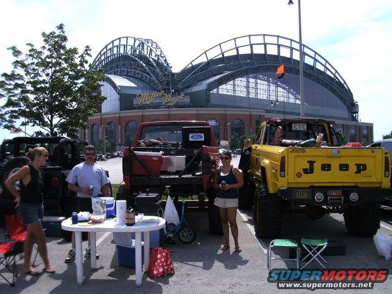 Yellow Jeep pickup and red Ford pickup trucks parked outside Miller Park stadium