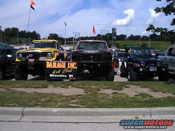 Yellow Jeep Cherokee, black Ford F-250, and blue Jeep Wrangler parked together with a 'Damage Inc. 4x4 Club' banner