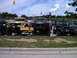 1994 Ford F-250 - Three lifted off-road vehicles are displayed with a club banner, under a partly cloudy sky.