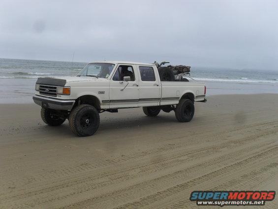 White 1991 Ford F-350 crew cab pickup truck with lifted suspension parked on a sandy beach near the ocean