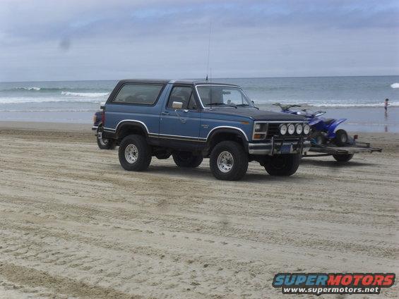 Blue SUV with black top on beach, towing ATV on trailer