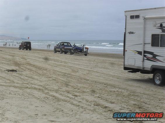 Pickup truck towing an ATV on the beach, with a Jeep and RV nearby