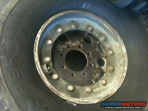 Close-up of a wheel with multiple lug nuts and a tire. Supermotors.net logo visible