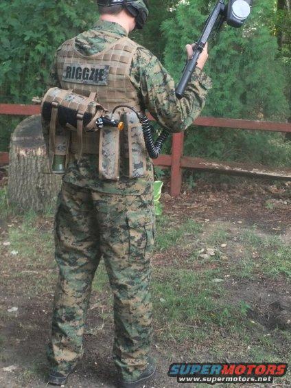 Person in camouflage gear with paintball gun and vest labeled 'RIGGZIE'