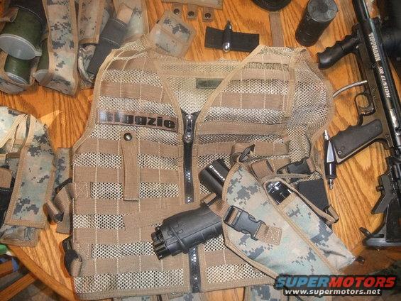 Tactical vest with "Illegazie" zipper pull, paintball gun, and various pouches on a wooden surface