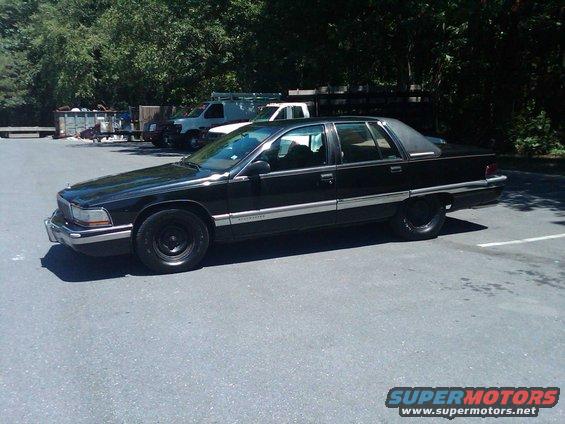 Black sedan parked in lot, other vehicles and trees in background. Badge reads 'Roadmaster'