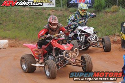 Two ATVs racing on a dirt track, one red and one white with number 238