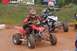 2004 Honda TRX 400 EX - Two riders compete in an ATV race on a dusty track, with spectators and banners in the background.