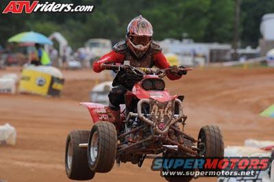 Red ATV airborne with rider, front view. ATVriders.com and Supermotors.net logos visible