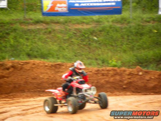 Red ATV with rider in helmet and red/black gear on a dirt track