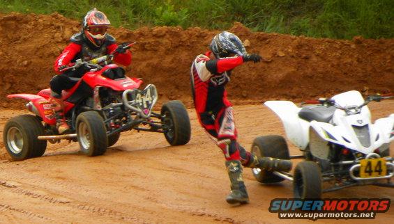 Red ATV with rider in front, white ATV with rider in middle on dirt track. Number 44 visible on white ATV