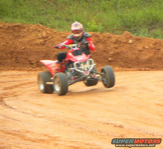 Red ATV with rider on a dirt track, front wheel lifted