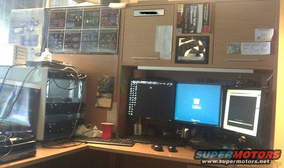 Office desk with multiple computer monitors, servers, posters, and books