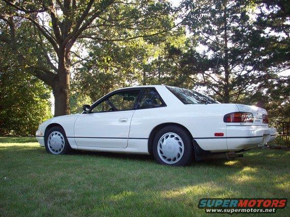 White coupe parked on grass, rear three-quarter view. Hubcaps visible