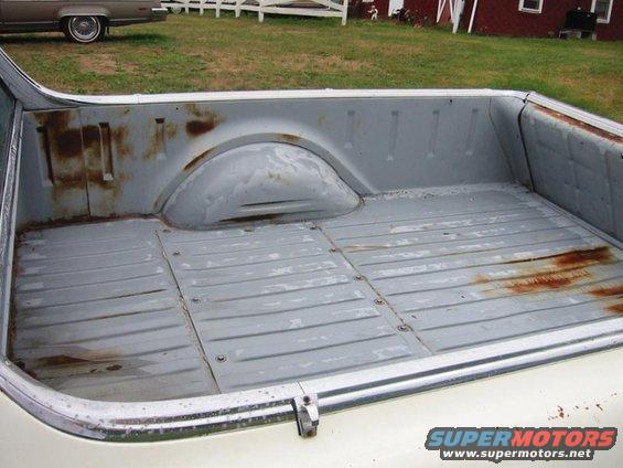 bed of a pickup truck with rust spots and a car in the background