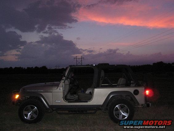 Tan Jeep Wrangler Rubicon with doors removed, parked in a field at dusk