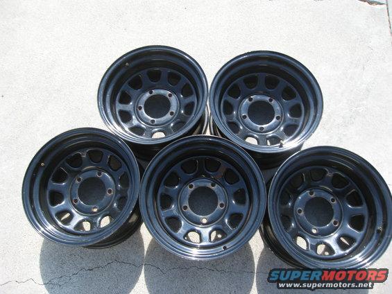 Five black steel wheels with a multi-hole design are laid out on a concrete surface