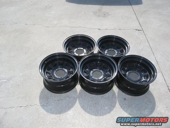 Five black steel wheels with chrome trim rings, laid out on concrete