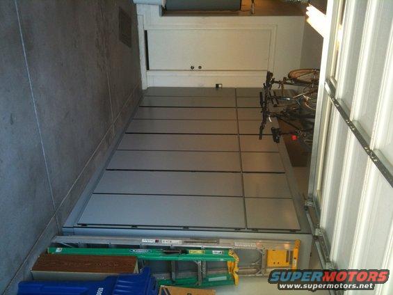 Garage interior with a gray floor, white cabinets, bicycles on a rack, and a ladder