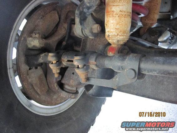 Close-up of rusty front suspension and steering linkage with a shock absorber and tire visible