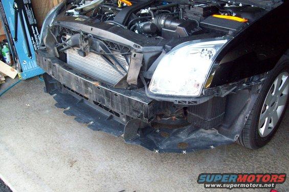 Black car front bumper removed, showing radiator and engine components. Visible wheel and headlight