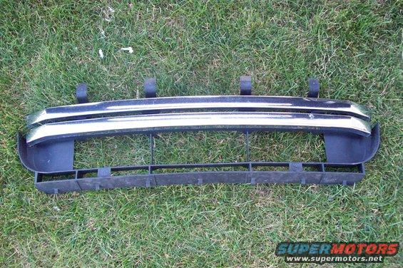 Car front bumper grille with chrome trim and black plastic lower section, lying on grass