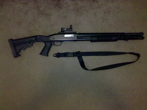 Tactical shotgun with adjustable stock, red dot sight, and sling laid out on carpet
