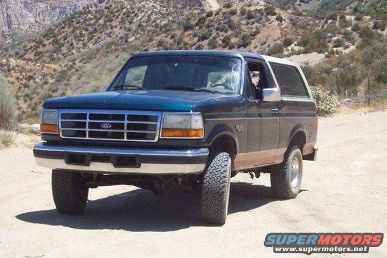 Green Ford Bronco parked on a dirt road with hills in the background