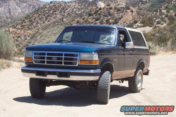 Dark green and tan Ford Bronco parked on a dirt road with mountains in the background