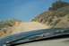 1995 Ford Bronco - View from inside a vehicle driving on a dusty, uphill dirt road with sparse vegetation under a clear blue sky.