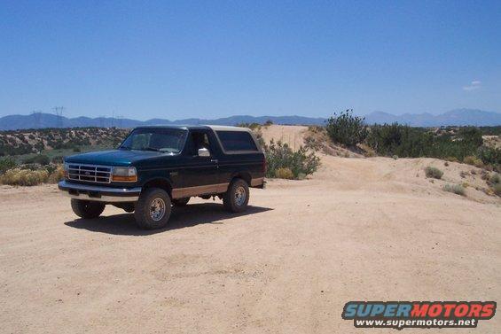 Green Ford Bronco parked on a dirt road with hills and power lines in the background