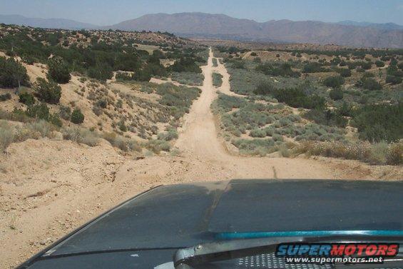 Vehicle dashboard and hood on dirt road with desert landscape