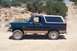1995 Ford Bronco - Side view of a green 1995 Ford Bronco with tan trim parked on a dirt road.