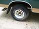 1989 Ford Bronco - The rear wheel and fender of a green and tan truck are visible, with dual exhaust pipes protruding from under the mud flap.