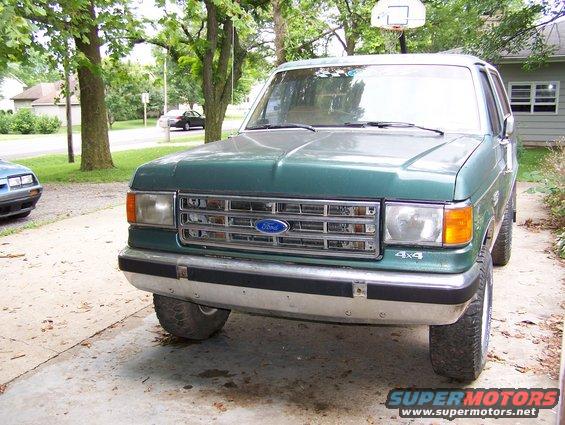Green Ford Bronco front view, chrome grille, 4x4 badge, parked on driveway