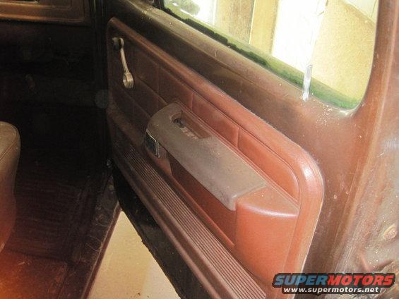 Interior view of a brown door panel with a window crank and armrest