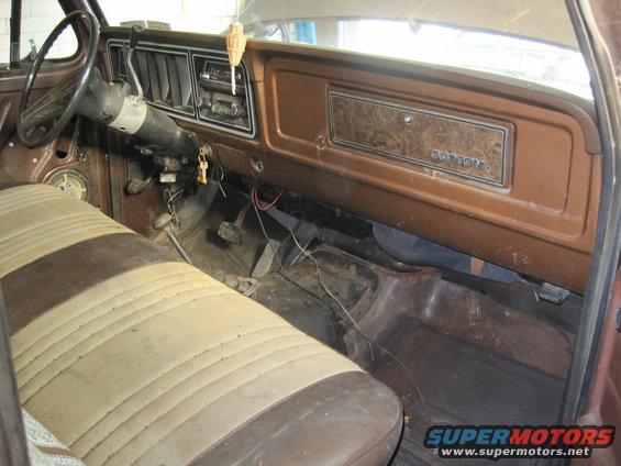 Interior shot of a vehicle's dashboard and front seat. Woodgrain trim on the dash says "CUSTOM"
