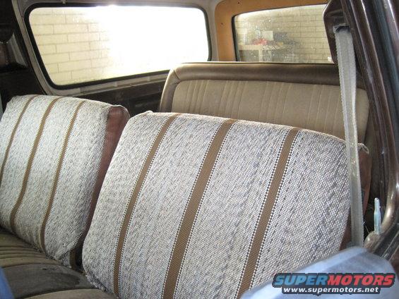 Rear bench seat with striped upholstery inside a vehicle. A seatbelt is visible