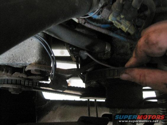 Close-up of engine bay with a hand adjusting a belt or pulley