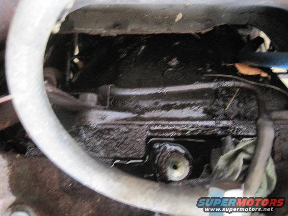 Close-up of a greasy engine oil pan with hoses and a rag