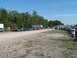 1985 Ford Mustang - A collection of vehicles are parked on a gravel lot under a clear blue sky, with trees and trailers visible.