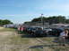 1985 Ford Mustang - A line of Ford Mustangs are parked on a gravel lot next to a race track fence.