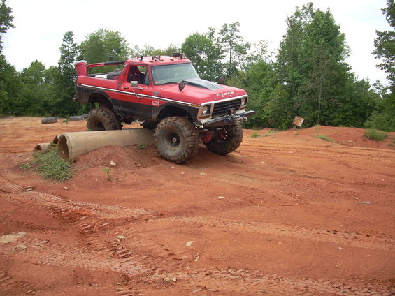 Red 1979 Ford Bronco with black hood stripe on off-road course