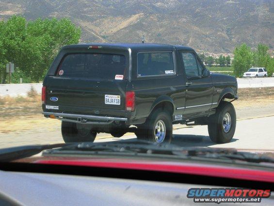 Black Ford Bronco with lifted suspension driving on a highway. Another white SUV is visible in the distance