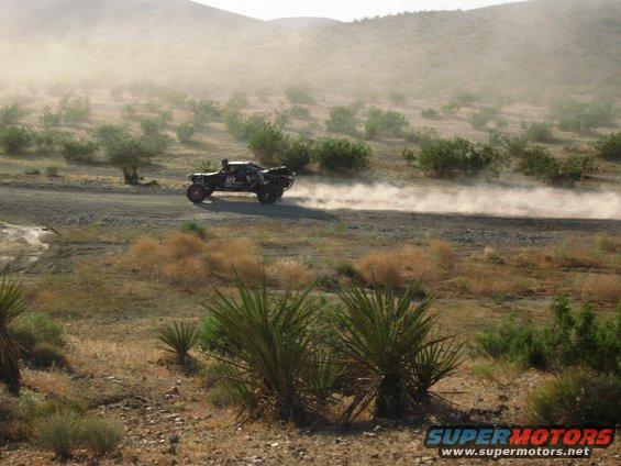 Off-road truck kicking up dust on a dirt road in a desert landscape