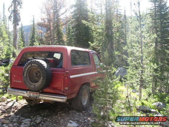 Red Ford Bronco parked on rocky trail in forest, spare tire mounted on rear door