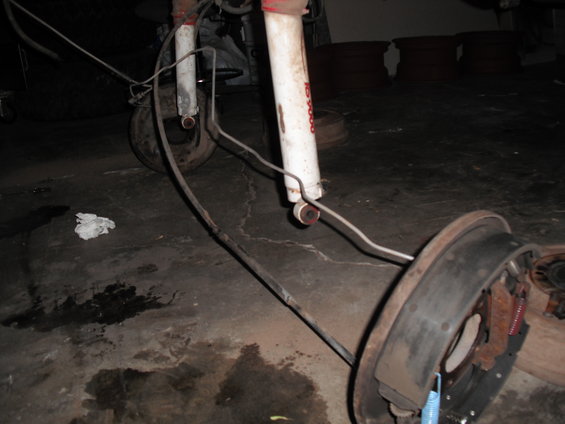 Rear axle assembly with brake drum, shock absorber, and brake lines on a concrete floor