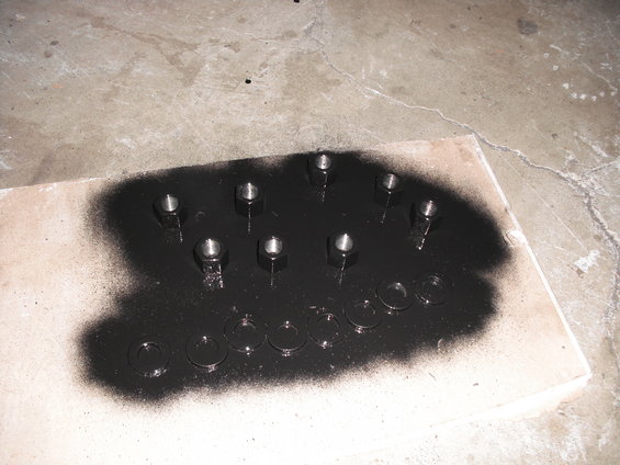 Nuts and washers on a piece of wood, partially covered in black spray paint