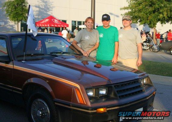 Brown 1979 Ford Mustang with gold trim, hood scoop, and a flag on the windshield