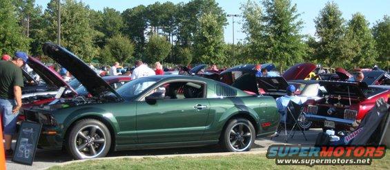 Green Ford Mustang coupe with hood open, parked at a car show with other vehicles